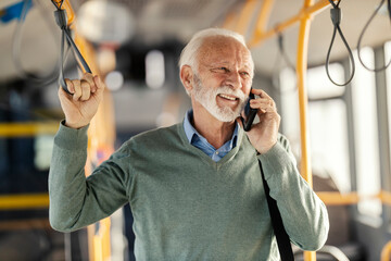 Portrait of smiling old passenger riding city bus and having phone conversation.