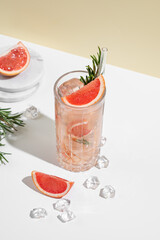 Refreshing cocktail with grapefruit, rosemary and ice in a glass on a white yellow background with shadow.