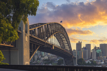 Obraz premium iconic steel arch bridge at sunset with city skyline in the background