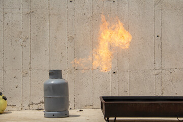 A gray gas cylinder in the open air, with flames shooting out of it