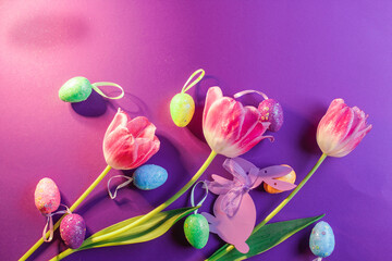 Easter eggs and tulips on purple background. Top view.