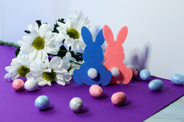 Easter decoration with eggs, rabbits and daisies on a purple background