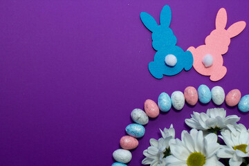 Easter decoration with eggs, bunny and flowers on purple background.