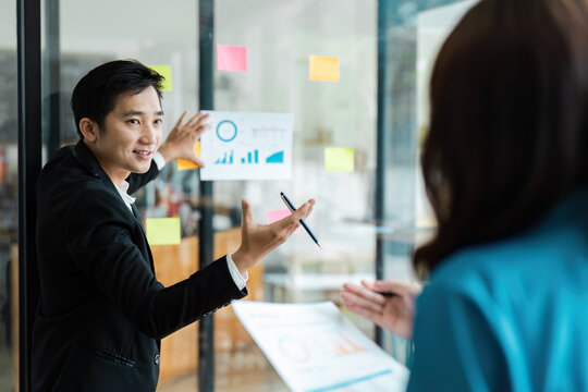 Business professional presenting financial data on a glass board, engaging in team collaboration.