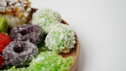 Various market snacks consisting of klepon, awug, jalabria, getuk, putu mayang and cikak are served on a wooden plate lined with banana leaves placed on a white base and background (isolated white).