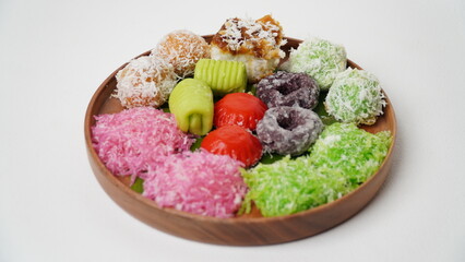 Various market snacks consisting of klepon, awug, jalabria, getuk, putu mayang and cikak are served on a wooden plate lined with banana leaves placed on a white base and background (isolated white).