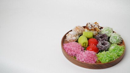 Various market snacks consisting of klepon, awug, jalabria, getuk, putu mayang and cikak are served on a wooden plate lined with banana leaves placed on a white base and background (isolated white).