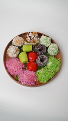 Various market snacks consisting of klepon, awug, jalabria, getuk, putu mayang and cikak are served on a wooden plate lined with banana leaves placed on a white base and background (isolated white).
