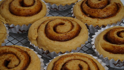 A collection of cinnamon rolls using paper cups and placed on a cooling rack with a white background (isolated white).