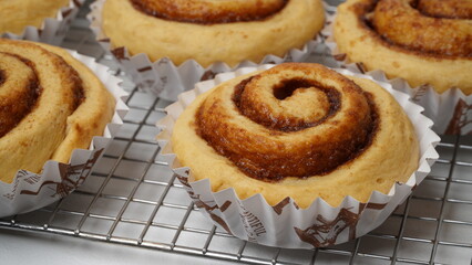 A collection of cinnamon rolls using paper cups and placed on a cooling rack with a white background (isolated white).