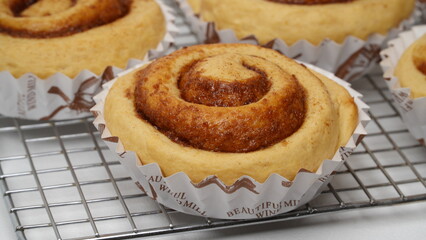 A collection of cinnamon rolls using paper cups and placed on a cooling rack with a white background (isolated white).
