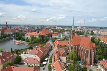 Obraz premium This aerial view of Wroclaw showcases its historic charm, featuring iconic red-roofed buildings a majestic Gothic church, and canals winding through the cityscape. 