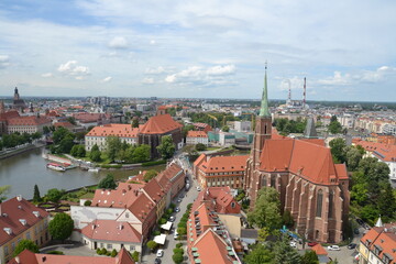 Fototapeta premium This aerial view of Wroclaw showcases its historic charm, featuring iconic red-roofed buildings, a majestic Gothic church, and canals winding through the cityscape. A perfect blend of history