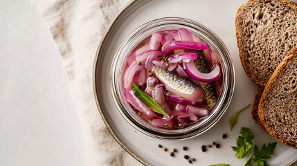 Norwegian sursild, pickled herring,  in a clear glass jar. Next to the jar, slices of dark, rye bread rest on a plain ceramic plate.