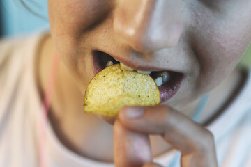 Closeup,bad food,asian little child girl eating potato chips,young woman puts crisps potato chip in...