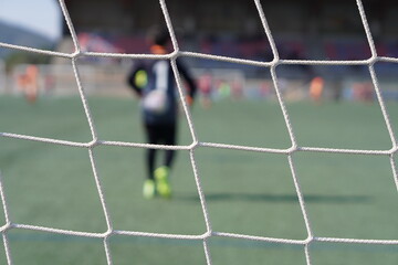 children's soccer. soccer goal net with goalkeeper and players out of focus in the background.