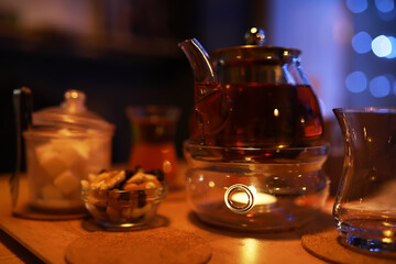 Evening Tea Setup: Glass Teapot with Warm Lighting and Assorted Snacks