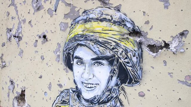 A close-up of a mural depicting a Ukrainian soldier, surrounded by real bullet and shrapnel holes, on a war-damaged building in Irpin, Ukraine, during the Ukraine-Russia conflict.