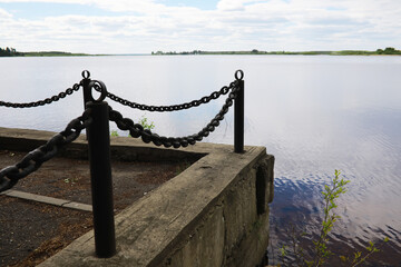 Tranquil Lakeside View with Chain Fence Along Concrete Path on Cloudy Day