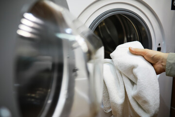 Person Loading White Laundry into Modern Front-Loading Washing Machine in Home Laundry Room