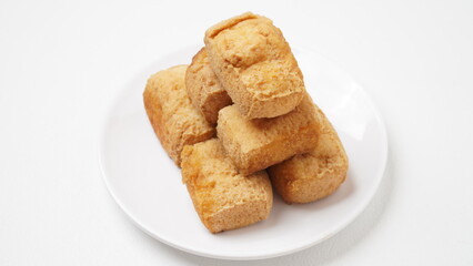 A portion of food called tahu pong is served using a white plate placed on a white place and background (isolated white).