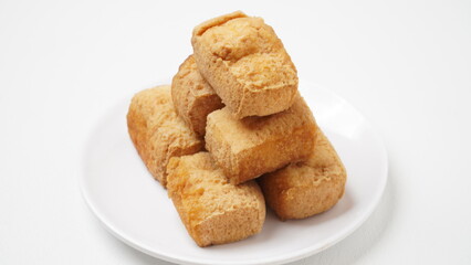 A portion of food called tahu pong is served using a white plate placed on a white place and background (isolated white).