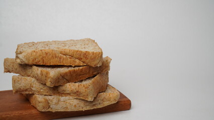 A stack of whole wheat bread served on a brown wooden board placed on a white background (isolated white).
