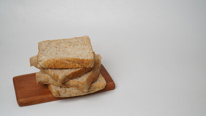 A stack of whole wheat bread served on a brown wooden board placed on a white background (isolated white).
