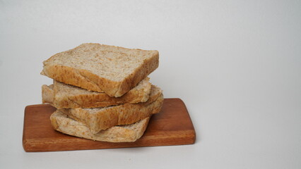 A stack of whole wheat bread served on a brown wooden board placed on a white background (isolated white).