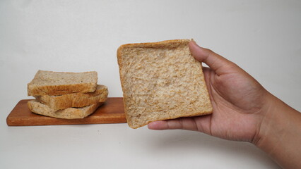 A hand holding a slice of whole wheat bread with a pile of bread beside it and a white background (isolated white).