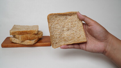 A hand holding a slice of whole wheat bread with a pile of bread beside it and a white background (isolated white).