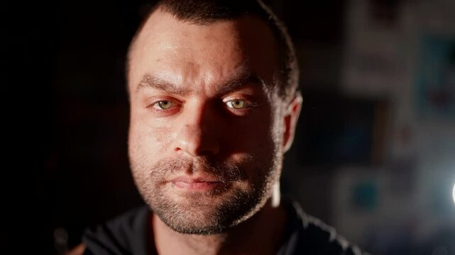 Male portrait with dramatic lighting. Half of the face is illuminated, emphasizing the harsh look and skin texture. A dark background enhances the effect of depth and contrast.