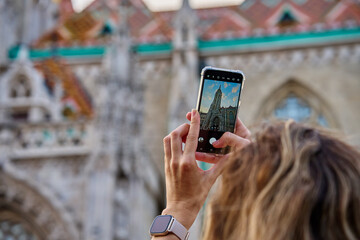Female tourist capturing photo of historic cathedral in Budapest using smartphone. Traveler walking...