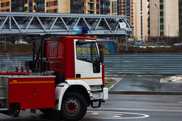 Red and white fire truck with extended ladder and flashing blue lights parked on the street near...