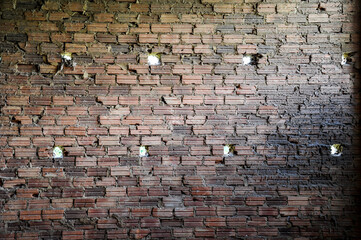 old brick wall inside house with holes to illuminated exterior
