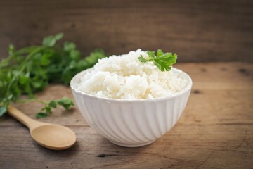 Cooked white rice or steamed rice in a white bowl with wooden spoon on wooden background