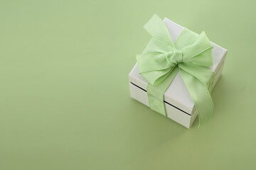 white gift box with green bow on green background with copy space.