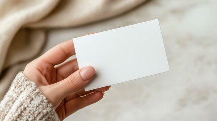 Hand holding blank business card with cozy sweater and neutral background