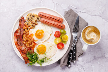 A classic breakfast plate featuring sunny-side-up eggs, crispy bacon, sausages, and fresh tomatoes