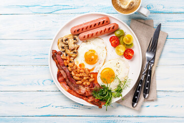 A classic breakfast plate featuring sunny-side-up eggs, crispy bacon, sausages, and fresh tomatoes