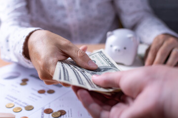 Person's hand delivering dollars savings bill to pay another person's hand.