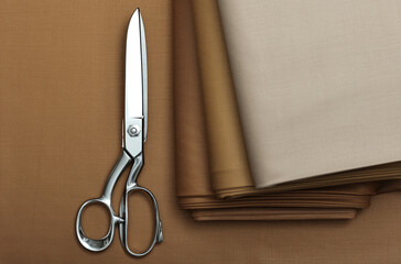 Top down view of earthy colors of cashmere, suiting fabric with metallic scissors on top of a table in fashion design studio.