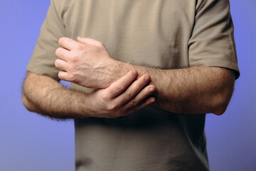 Fototapeta premium A man holds his wrist in pain. The hand tightly clasps the affected area, emphasizing the soreness and need for support. Pain and suffering in the wrist interfere with professional activities.