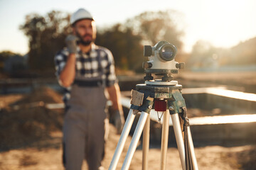 With geodetic optical level. Worker is on the construction site at daytime