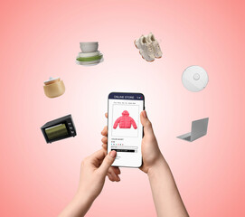 Woman holding mobile phone with open online store website surrounded by different goods on pink...