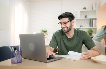 Portrait of a young freelancer smiling while working online via laptop at home with his girlfriend