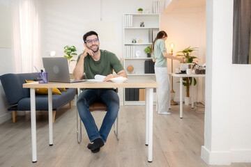 Portrait of a young freelancer smiling while working online via laptop at home with his girlfriend