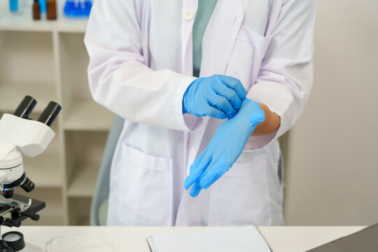 Caucasian school children learning experiment in science classroom. Young female scientist wearing a white lab coat and blue gloves putting on safety gear before conducting a chemistry experiment.