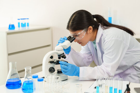 Caucasian school children learning experiment in science classroom. Young female scientist in lab coat using microscope while conducting a biology experiment, demonstrating curiosity and focus.