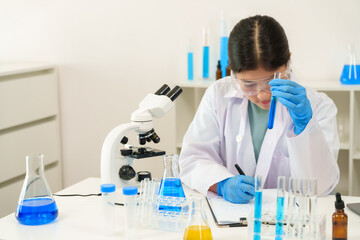 Caucasian school children learning experiment in science classroom. Young female student in lab coat using a pipette to transfer liquid into test tube, demonstrating precision in chemistry experiment.